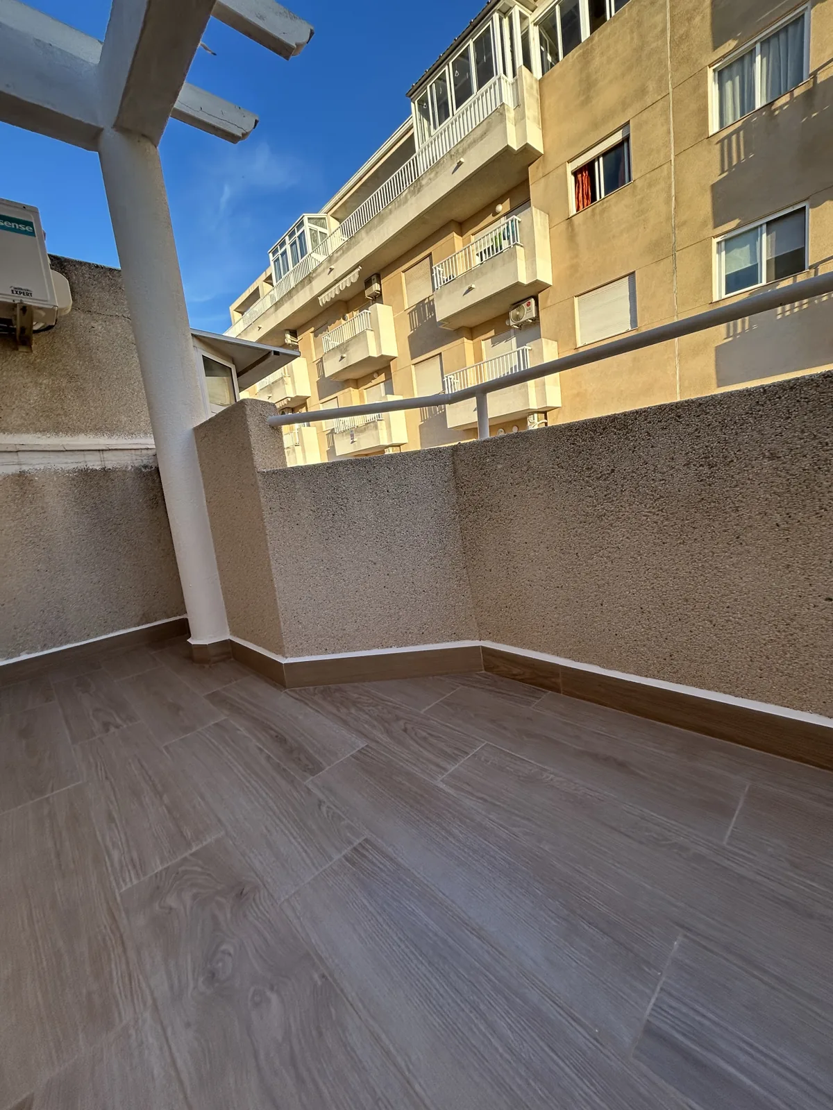 Balcón reformado con azulejo madera y techo pergola